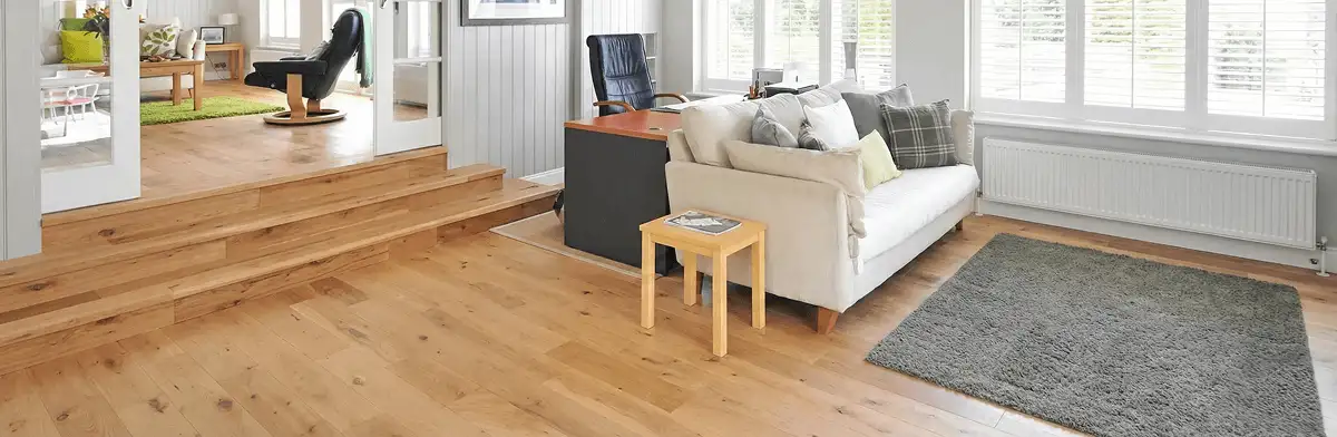 A modern living room with professionally installed laminate flooring, a beige sofa, a small side table, a gray rug, and large windows with white shutters in Pueblo, CO
